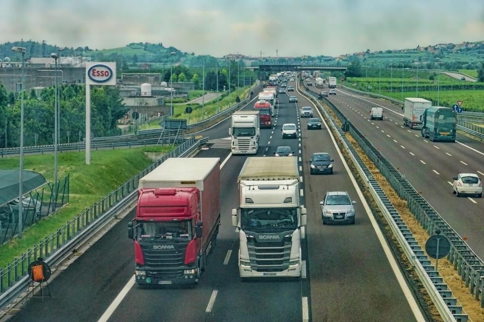 A imagem demonstra duas rodovias e caminhões transportando mercadorias